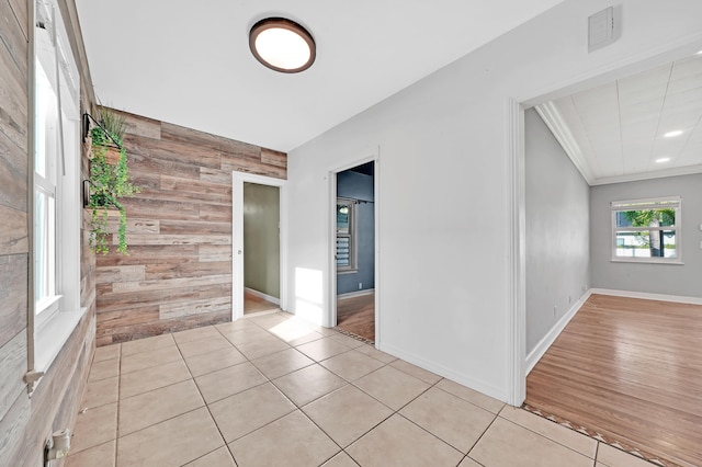 empty room with light hardwood / wood-style floors, wood walls, and crown molding