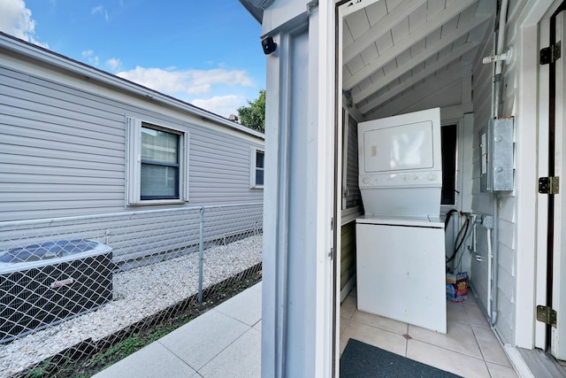 laundry area featuring wooden walls, stacked washer and clothes dryer, and light tile patterned floors