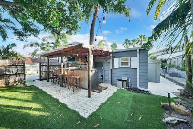 rear view of house featuring a patio area, a storage unit, a lawn, and exterior bar