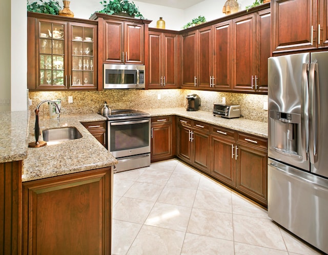 kitchen featuring stainless steel appliances, sink, light stone counters, and backsplash