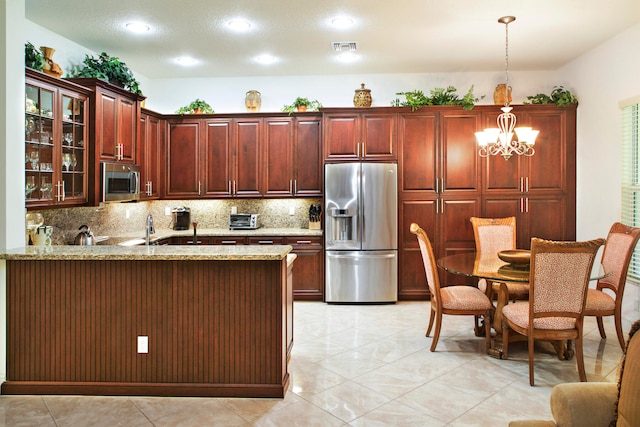 kitchen with light stone counters, stainless steel appliances, hanging light fixtures, decorative backsplash, and a chandelier