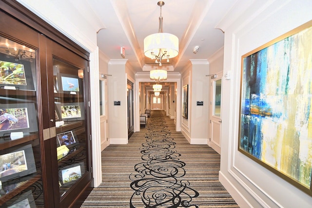 hallway featuring a chandelier, a tray ceiling, dark carpet, and crown molding