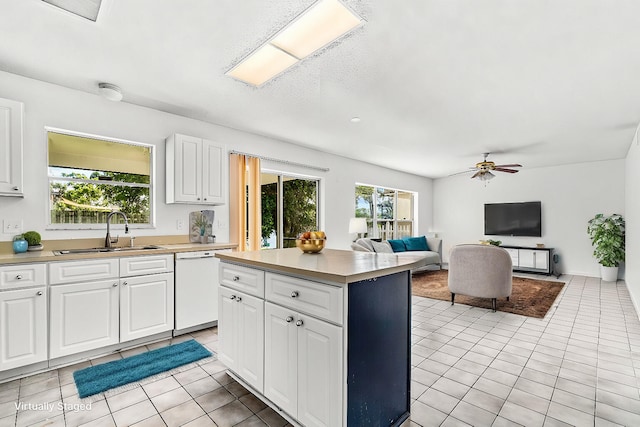 kitchen featuring a kitchen island, white dishwasher, sink, light tile patterned floors, and white cabinetry