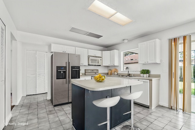 kitchen with white cabinets, light tile patterned floors, a kitchen island, a breakfast bar, and white appliances