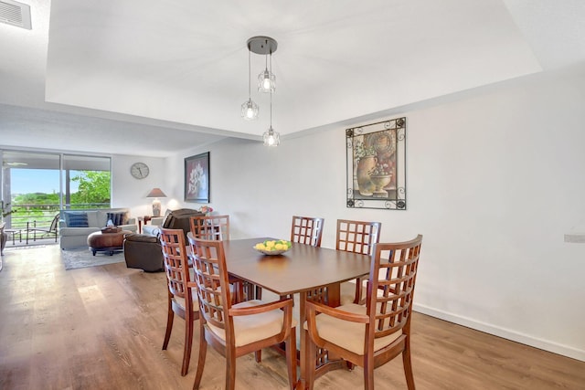 dining space with wood-type flooring and a tray ceiling