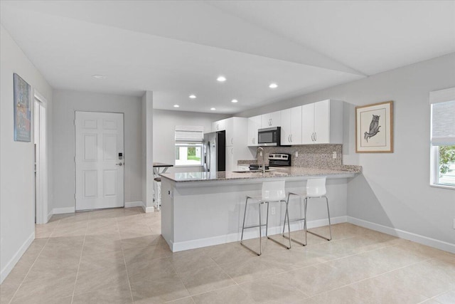 kitchen with kitchen peninsula, a breakfast bar, white cabinets, light tile patterned floors, and appliances with stainless steel finishes