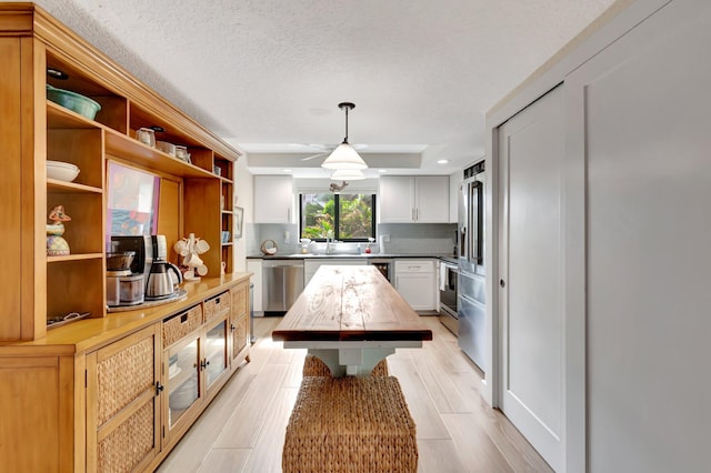 kitchen with a center island, white cabinets, pendant lighting, appliances with stainless steel finishes, and a textured ceiling