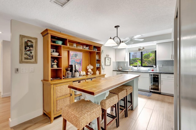 kitchen featuring white cabinets, beverage cooler, a kitchen breakfast bar, wood counters, and pendant lighting