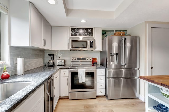 kitchen with a tray ceiling, stainless steel appliances, white cabinetry, light stone counters, and light hardwood / wood-style floors