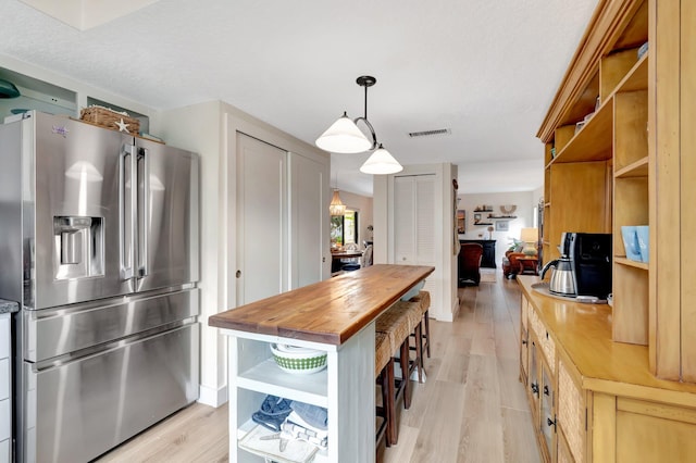 kitchen featuring butcher block countertops, light hardwood / wood-style flooring, pendant lighting, and stainless steel refrigerator with ice dispenser