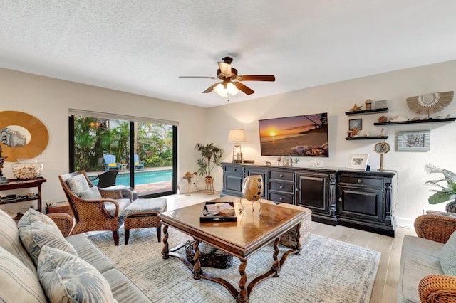 living room featuring a textured ceiling, light wood-type flooring, and ceiling fan