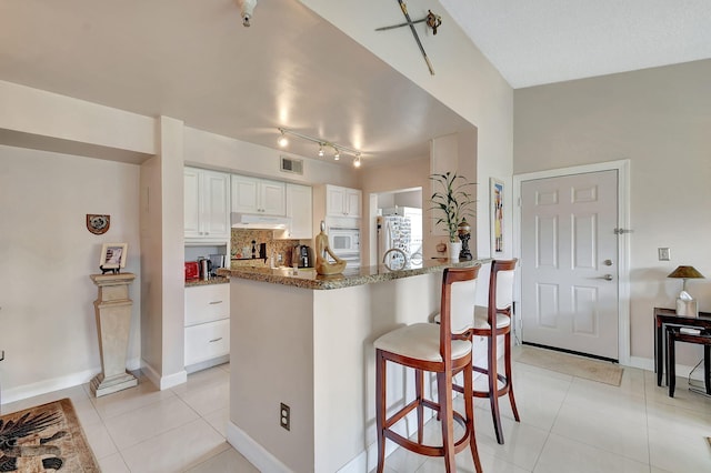 kitchen featuring light tile patterned floors, a kitchen breakfast bar, white cabinetry, light stone countertops, and white appliances