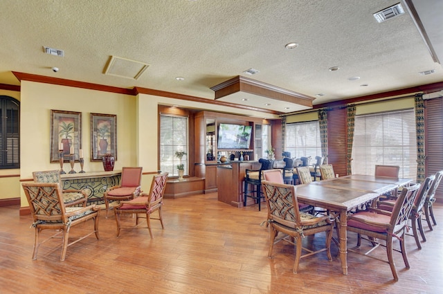 dining area with light hardwood / wood-style floors, a textured ceiling, and ornamental molding