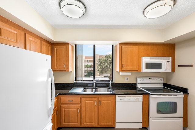 kitchen with sink, a textured ceiling, white appliances, and dark stone countertops