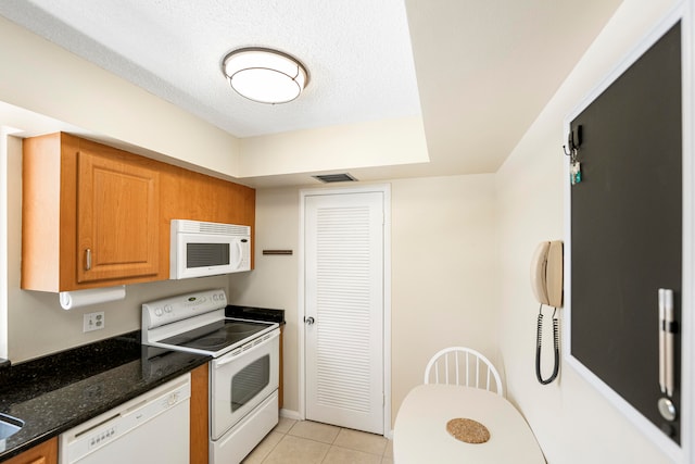 kitchen with light tile patterned floors, a textured ceiling, white appliances, and dark stone countertops