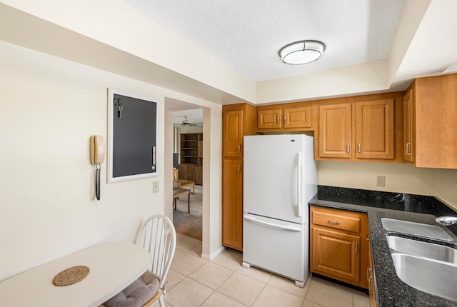 kitchen featuring light tile patterned flooring, sink, a textured ceiling, dark stone counters, and white refrigerator