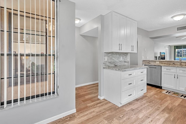 kitchen with white cabinets, stainless steel dishwasher, light wood-type flooring, and a textured ceiling