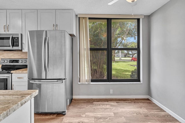 kitchen with light stone countertops, appliances with stainless steel finishes, a textured ceiling, and white cabinets