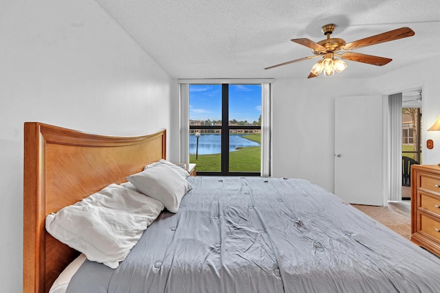 bedroom with multiple windows, a textured ceiling, a water view, and ceiling fan