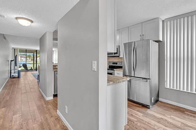 kitchen with appliances with stainless steel finishes, a textured ceiling, white cabinetry, light hardwood / wood-style floors, and light stone counters