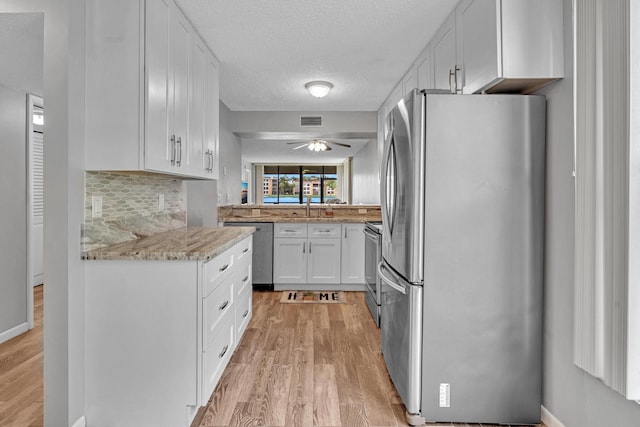 kitchen with decorative backsplash, white cabinets, ceiling fan, light hardwood / wood-style floors, and stainless steel appliances