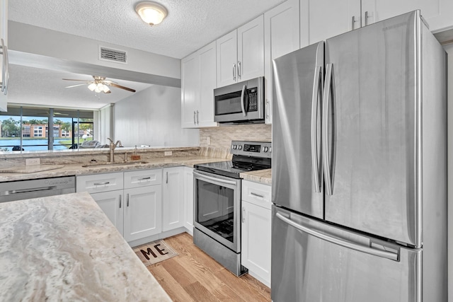 kitchen with sink, a textured ceiling, stainless steel appliances, white cabinets, and light hardwood / wood-style flooring