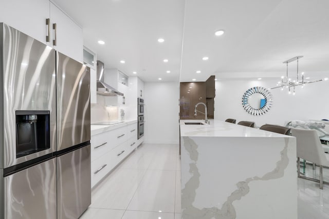 kitchen with appliances with stainless steel finishes, white cabinetry, a sink, wall chimney range hood, and modern cabinets