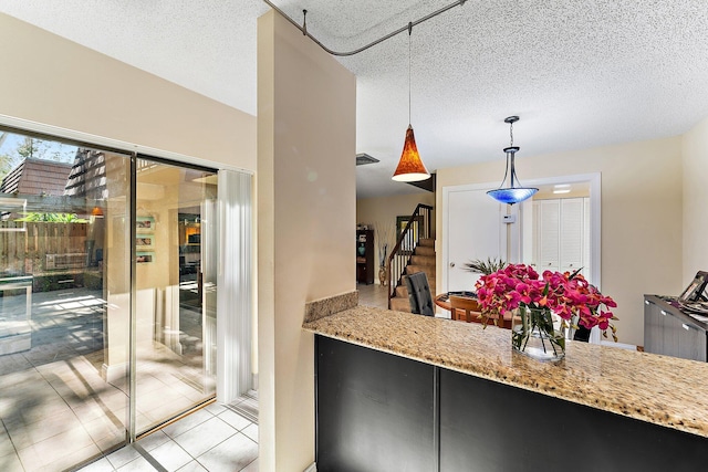 kitchen with light stone counters, a textured ceiling, light tile patterned floors, and pendant lighting