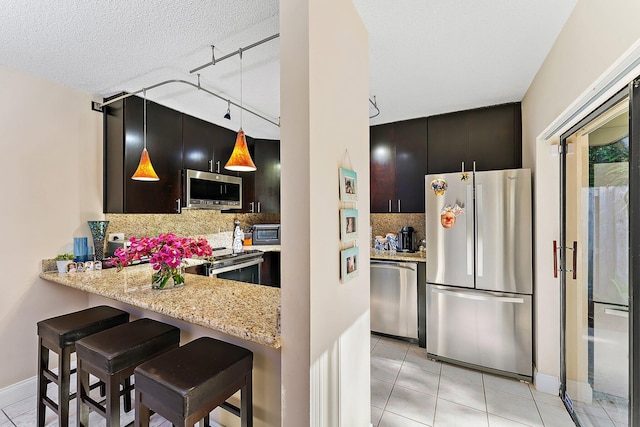 kitchen featuring kitchen peninsula, stainless steel appliances, decorative light fixtures, decorative backsplash, and a breakfast bar