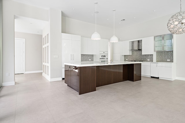 kitchen with wall chimney exhaust hood, a center island with sink, white cabinetry, and tasteful backsplash