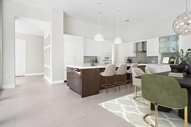 kitchen featuring pendant lighting, wall chimney exhaust hood, white cabinetry, and a kitchen island with sink