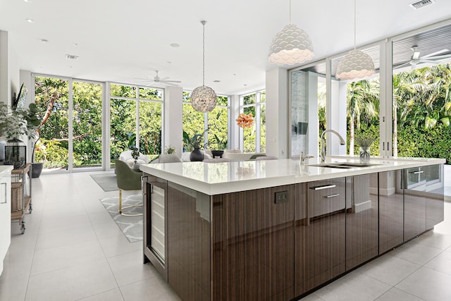 kitchen with light tile patterned flooring, sink, floor to ceiling windows, decorative light fixtures, and a large island