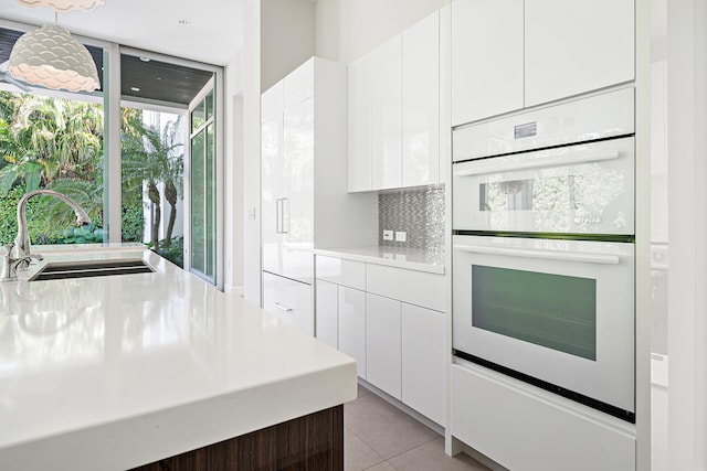 kitchen with white cabinetry, sink, tasteful backsplash, hanging light fixtures, and white double oven