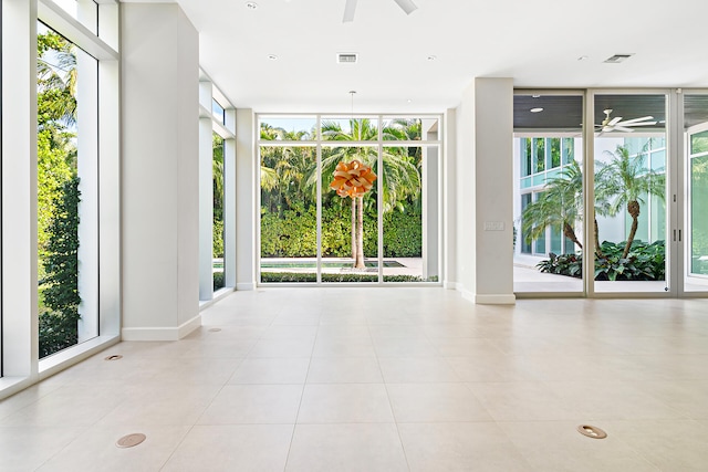 tiled empty room featuring ceiling fan and a wall of windows