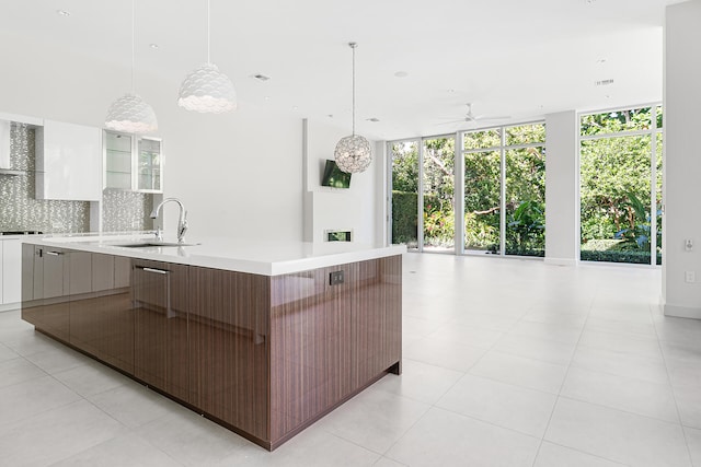 kitchen with sink, a wall of windows, decorative backsplash, white cabinets, and a spacious island