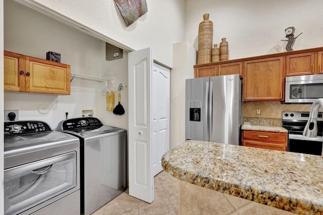 kitchen featuring washing machine and dryer, decorative backsplash, stainless steel appliances, and light tile patterned floors