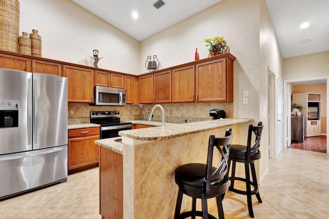 kitchen with light tile patterned flooring, kitchen peninsula, a kitchen breakfast bar, stainless steel appliances, and light stone counters