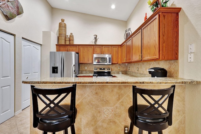 kitchen with lofted ceiling, stainless steel appliances, kitchen peninsula, and a breakfast bar area