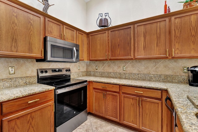 8503 Logia Cir, Boynton Beach, FL 33472 - kitchen featuring light stone countertops, brown cabinetry, light tile patterned flooring, tasteful backsplash, and appliances with stainless steel finishes