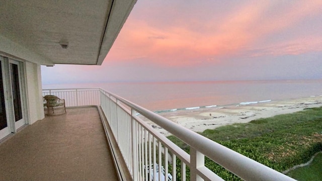 balcony at dusk featuring a water view and a view of the beach