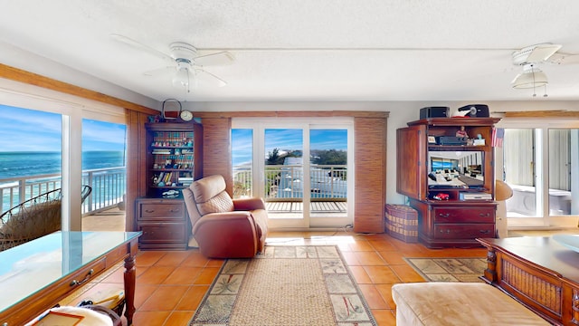 living room with a textured ceiling, ceiling fan, a water view, and light tile patterned floors