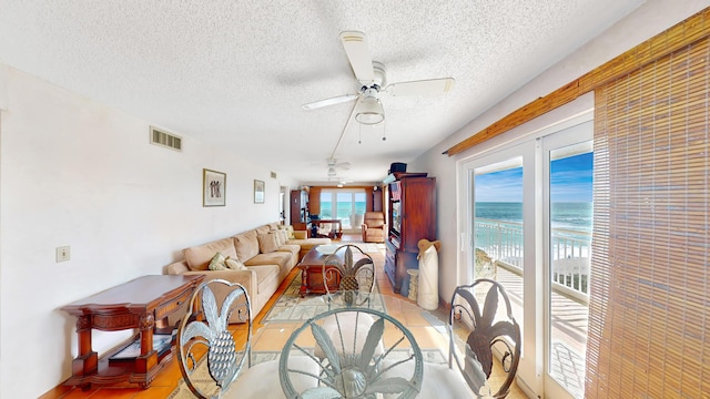 living room featuring ceiling fan, a water view, and a textured ceiling