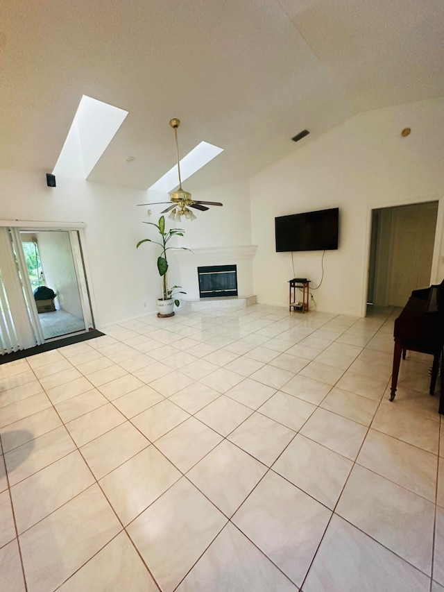 unfurnished living room with ceiling fan, vaulted ceiling with skylight, and light tile patterned floors