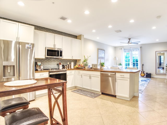 kitchen featuring kitchen peninsula, stainless steel appliances, light tile patterned flooring, white cabinetry, and ceiling fan