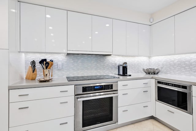 kitchen featuring white cabinetry, stainless steel appliances, tasteful backsplash, extractor fan, and light tile patterned floors