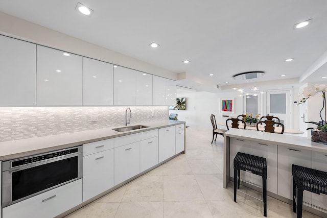 kitchen featuring decorative backsplash, sink, pendant lighting, white cabinetry, and light tile patterned flooring