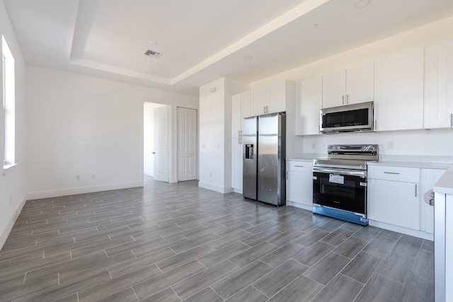 kitchen with stainless steel appliances, hardwood / wood-style flooring, white cabinetry, and a raised ceiling