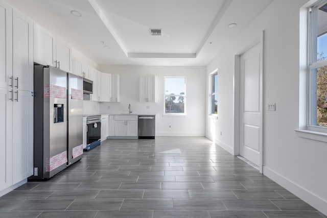 kitchen featuring visible vents, baseboards, a tray ceiling, white cabinets, and stainless steel appliances