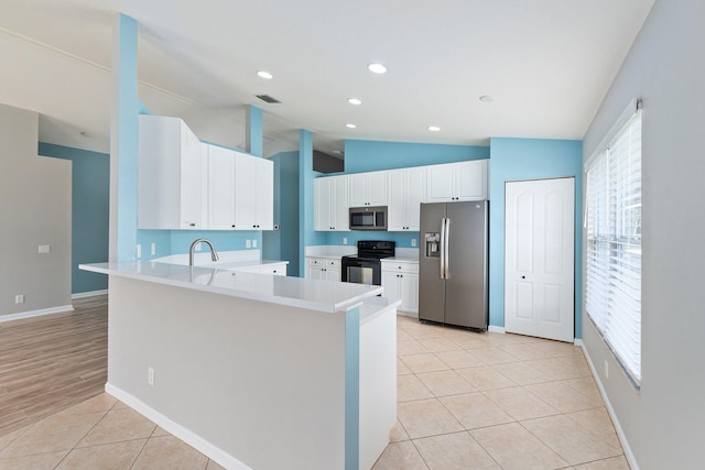 kitchen featuring lofted ceiling, kitchen peninsula, white cabinetry, light tile patterned floors, and appliances with stainless steel finishes