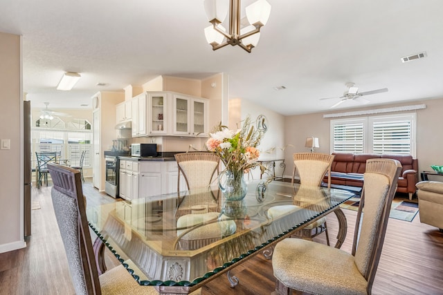 dining area with hardwood / wood-style flooring and ceiling fan with notable chandelier